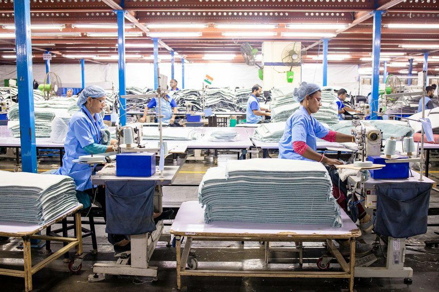 作業台に畳んだ布を積んで縫製をする人たち